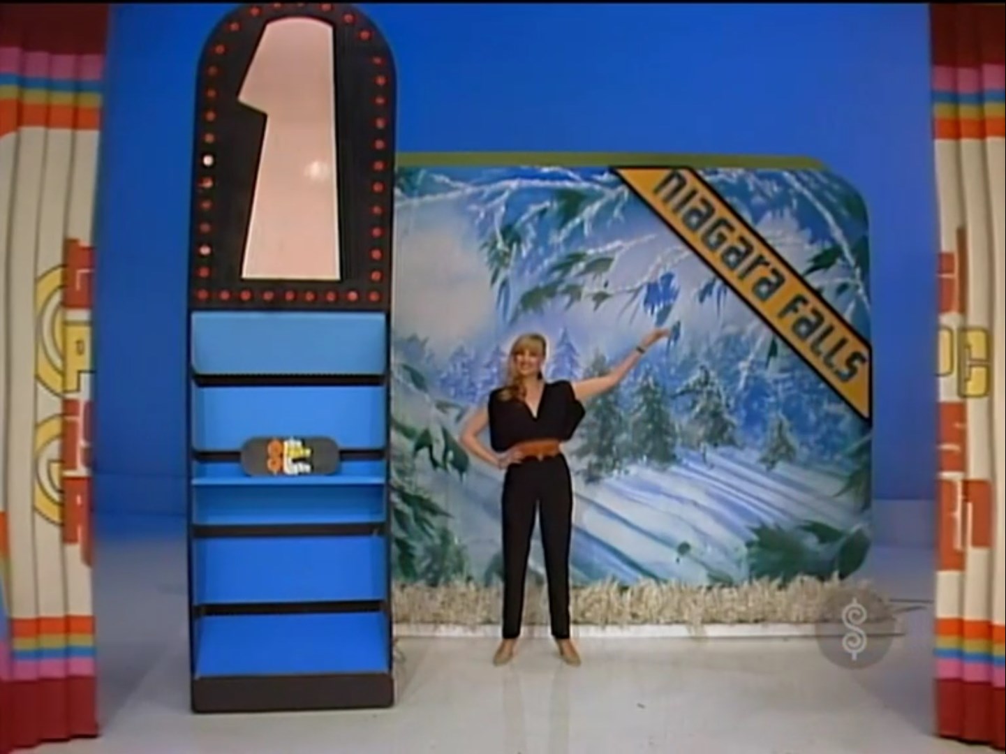 A model points to a sign for Niagara Falls while standing next to a game podium labeled '1' on the set of The Price Is Right.