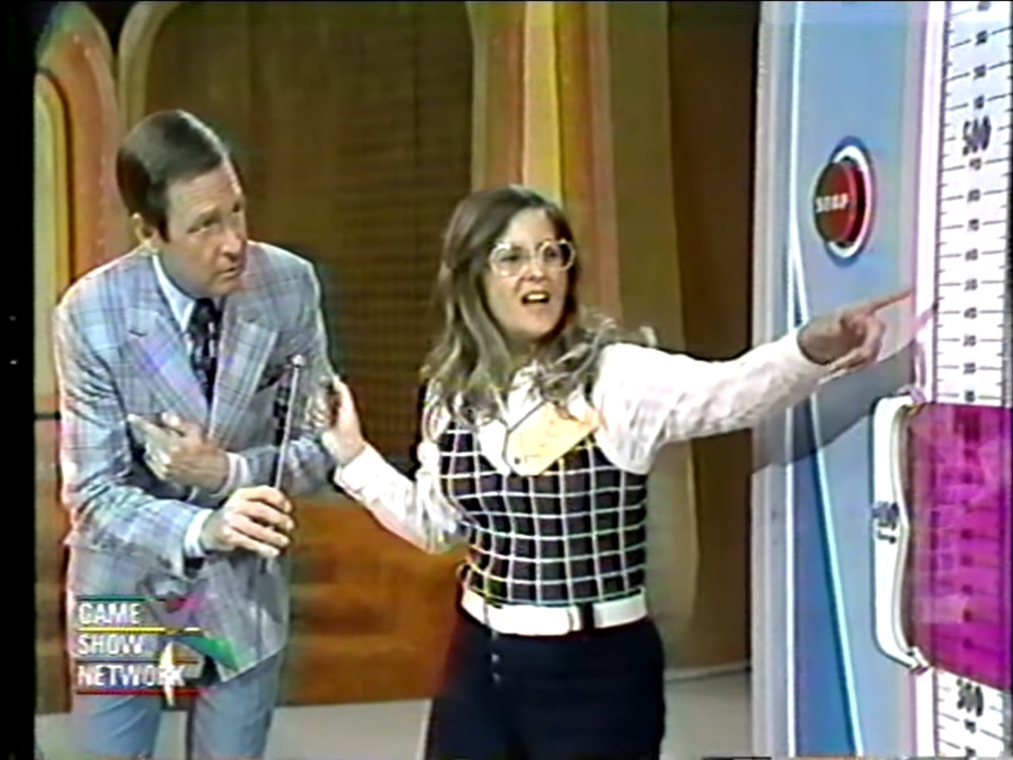 A contestant excitedly points to the price scale while a host listens attentively during the Range Game segment on a game show.