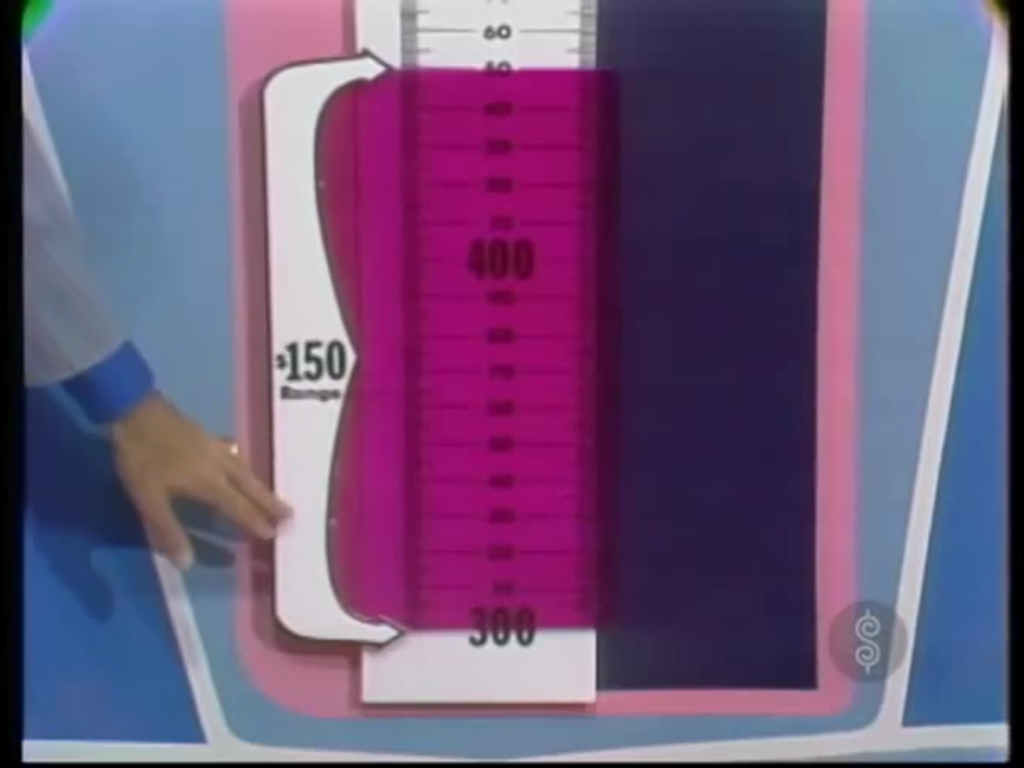 A close-up of the Range Game scale from The Price is Right, featuring a 0 range finder in a pink translucent window, with a hand pointing at it.