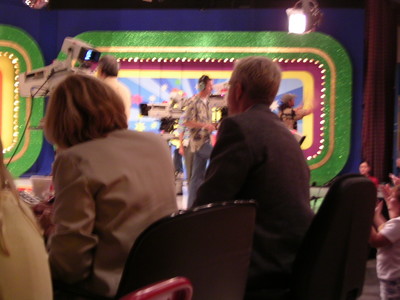 View of the stage during a taping of a television show, with crew members and audience members visible in the foreground.