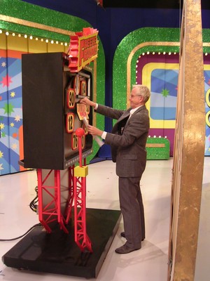 A man in formal attire operating a colorful game show wheel in a vibrant studio setting.