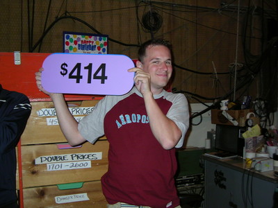 A person smiling and holding a purple sign with the number $414 in a backstage setting.