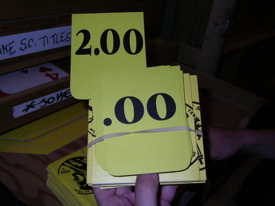 A person's hand holding a stack of yellow cards with large black numbers, including "2.00" at the top, on a wooden surface.