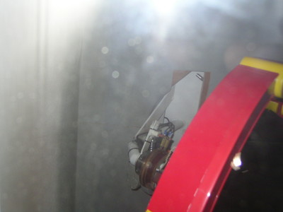 A close-up of a mechanical component behind a glass enclosure, with reflections obscuring the view.