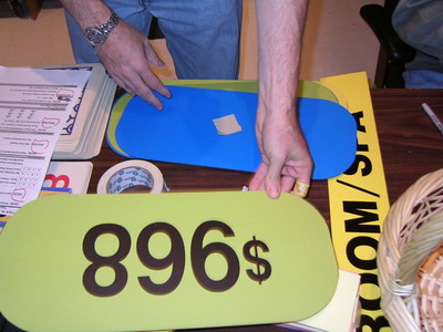 A person is placing a green sign with the number '896$' on a table, surrounded by other signs and supplies.