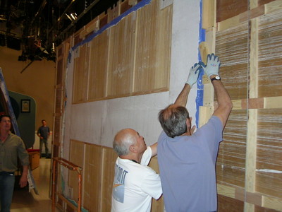 Two crew members working on a set wall during the backstage preparations for a premiere.
