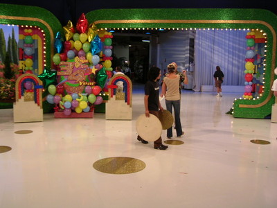 Backstage at a television studio during the Season 34 premiere, featuring colorful decorations, including balloons and a festive sign, with crew members preparing for the show.