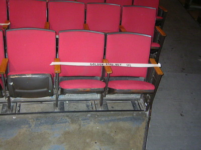 Empty red theater seats with a sign that reads 'GOLDEN-ROAD.NET' across the armrest.