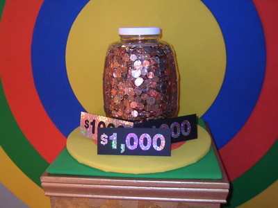 A jar filled with coins sits on a colorful pedestal with signs displaying '$1,000'.