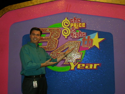 Rich Fields stands beside a decorative backdrop celebrating the 34th year of 'The Price is Right', featuring colorful text and stars.