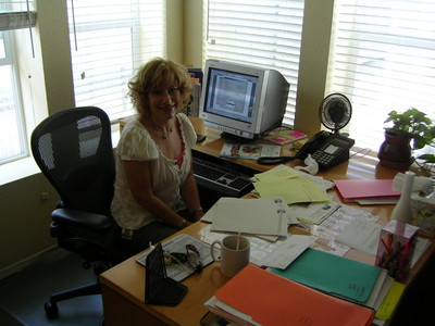 Karen Wohlmuth sitting at a cluttered desk in an office with a computer and various documents.
