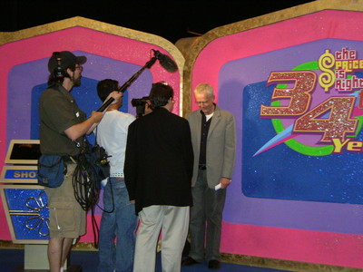 Filming behind the scenes at the premiere of Season 34 of The Price is Right, featuring a host speaking to the camera crew in front of vibrant set decorations.