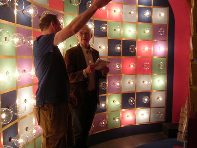 John Sly and Roger Dobkowitz engaged in conversation in front of a colorful, illuminated wall with circular light fixtures.