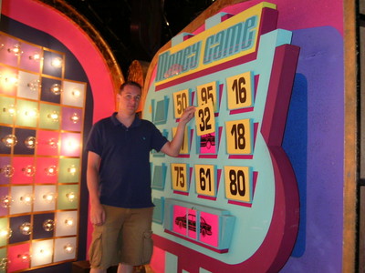 ClockGameJohn standing next to the 'Money Game' board featuring numbers and colorful design on a game show set.