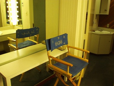 Director's chair with the name 'Bob' on it next to a vanity mirror in a dressing room.