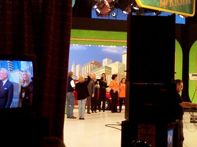 View of a television studio set with a live audience, featuring a group of people on stage and a television monitor in the foreground, taken from a show that aired in January 2000.
