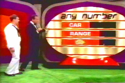 A scene from The Price is Right game show featuring the 'Any Number' game display, with a host and a contestant standing on stage. The set has newly debuted during the 1986 Primetime specials.