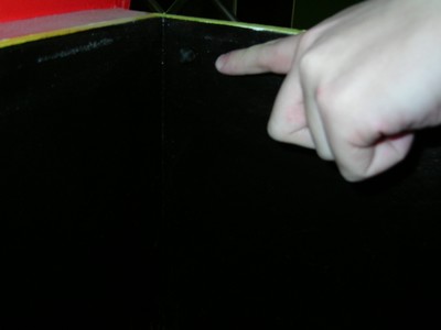 A close-up of a hand pointing at a corner of the inside of the Push Over box, with a microphone inside.