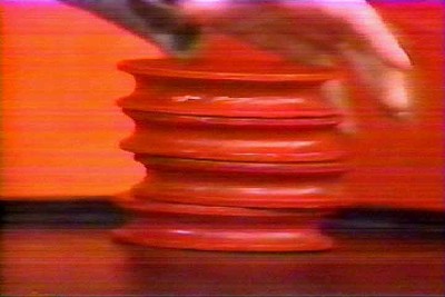 In the game Shell Game, a hand reaching towards a stack of red, circular chips on a table, set against a colorful background.