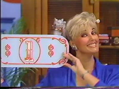 A smiling woman holding a game board with the number '1' and dollar signs, set in a vibrant studio background.