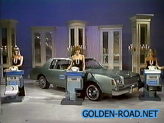 A vintage game show set featuring a green car and three contestants at podiums, with a backdrop of elegant decor.