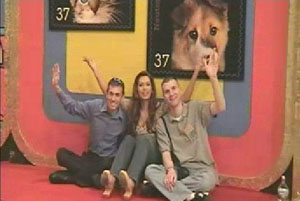 Jake Mangin, Brandi Sherwood, and Doug Bradshaw sitting on the floor in front of colorful backdrops featuring animal photographs, smiling and waving.