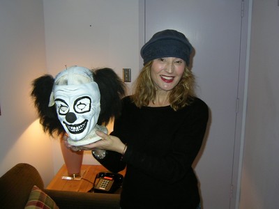 Mira Wilder wearing a hat is smiling while holding a clown mask with exaggerated features and black fur accents.