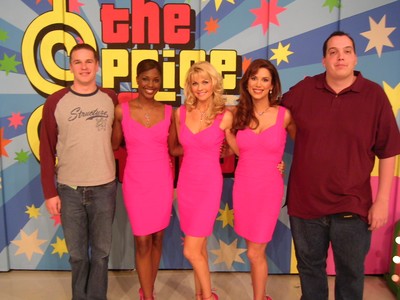 A group of four individuals, including two women in pink dresses and two men, pose in front of a colorful backdrop with the logo of 'The Price is Right'.