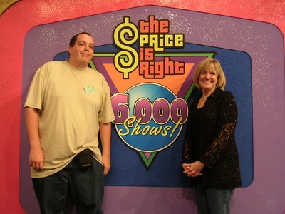 Kathy Greco and Marc Green standing beside 'The Price is Right' logo celebrating 6,000 shows, with a colorful backdrop.
