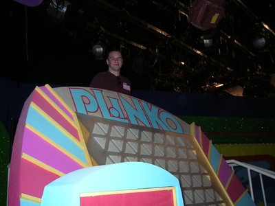A person stands at the Plinko game setup on The Price is Right stage, with colorful sections and the game board in the background.
