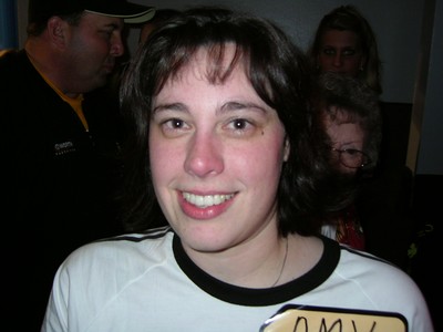 Amy Rempel, the winner of the 6,000th episode of The Price is Right, smiling for the camera, wearing a t-shirt with a black collar, and a name tag that reads 'AMY'.