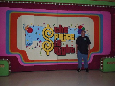 A person standing in front of a colorful backdrop featuring the logo of 'The Price is Right' game show.