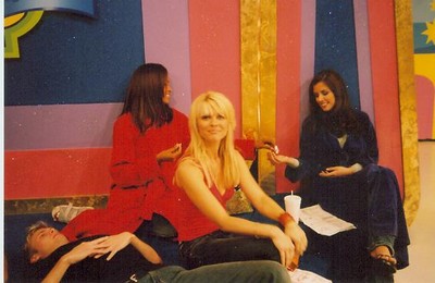 A group of individuals relaxing on set, with one person sitting in front and two other women seated nearby, dressed casually in colorful attire.