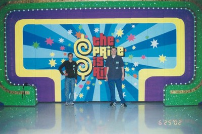 Two men posing in front of a colorful backdrop featuring The Price is Right logo.