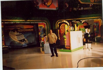 A backstage view of The Price is Right set, featuring colorful game elements and a man standing near a display board.