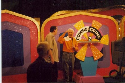 Scene from The Price is Right show featuring a colorful backdrop with the words 'COMING GOING' and two contestants interacting on stage.