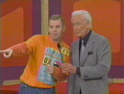 A contestant wearing an orange shirt points while standing next to a host during a game show segment on The Price is Right.