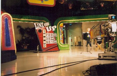 An interior view of Stage 33 at CBS Television City, showcasing the game show set of 'Line 'Em Up' with a bright and colorful backdrop and a camera on a tripod.