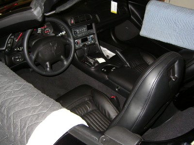 Interior view of a black sports car, featuring leather seats and a steering wheel, covered with protective blankets.