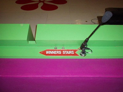 Close-up of a sign labeled 'Winners Stairs' on a green podium, with a microphone attached.