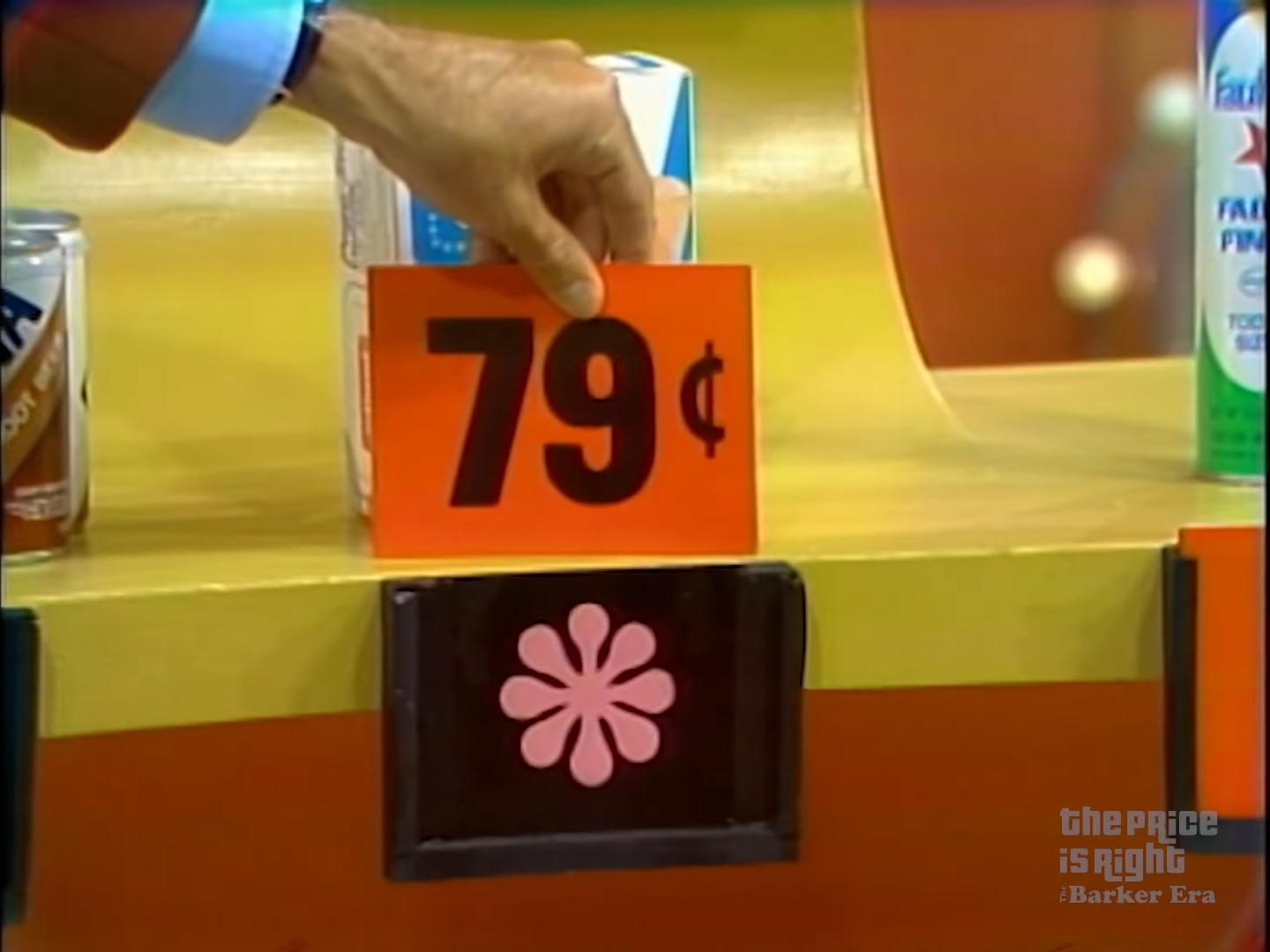 A hand holding a price tag reading '79¢' next to a display of grocery products on The Price Is Right game show.