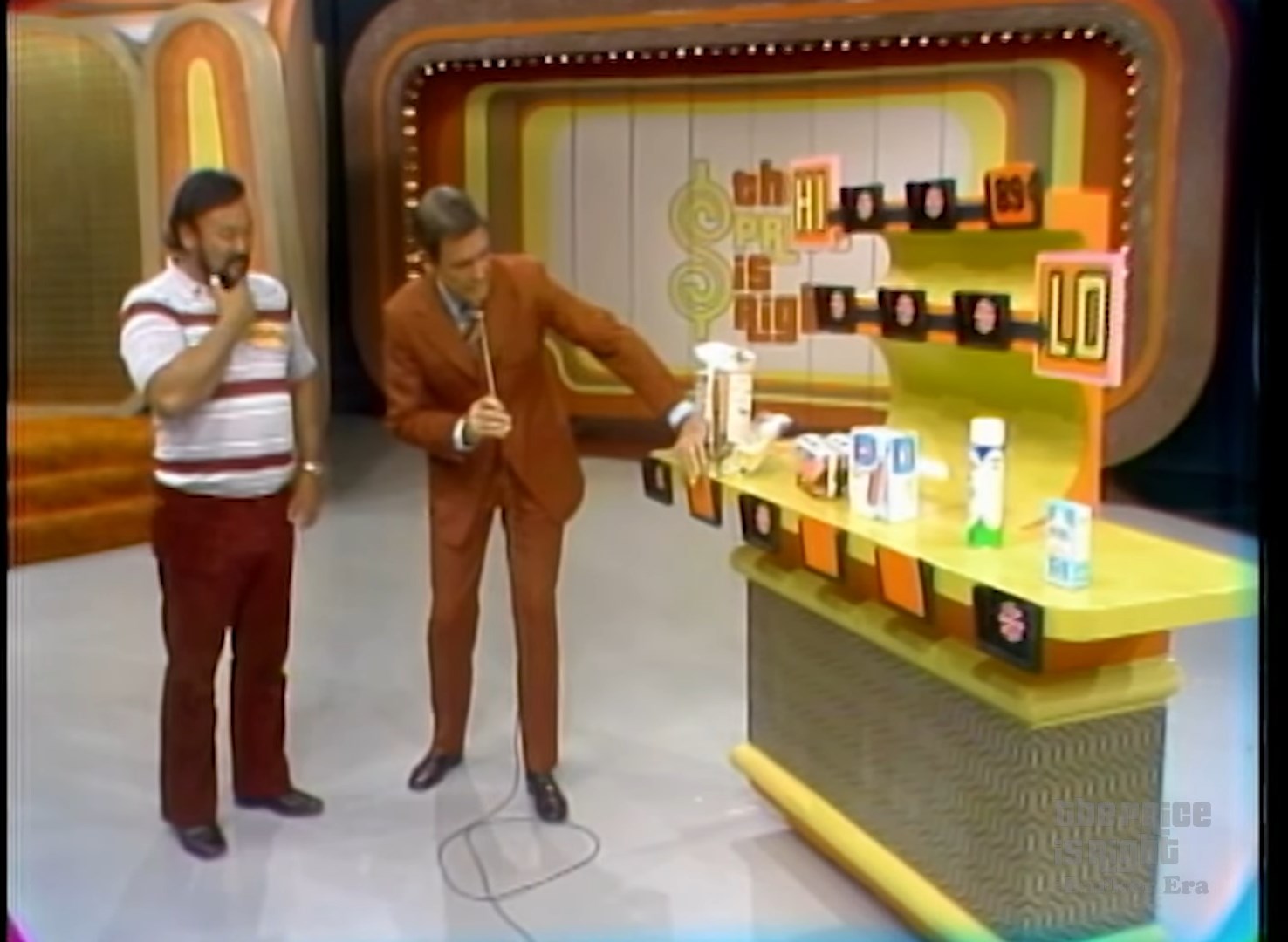 A contestant and host interacting in the Hi Lo game from The Price is Right, with various grocery products displayed on a game board labeled 'Hi' and 'Lo'.