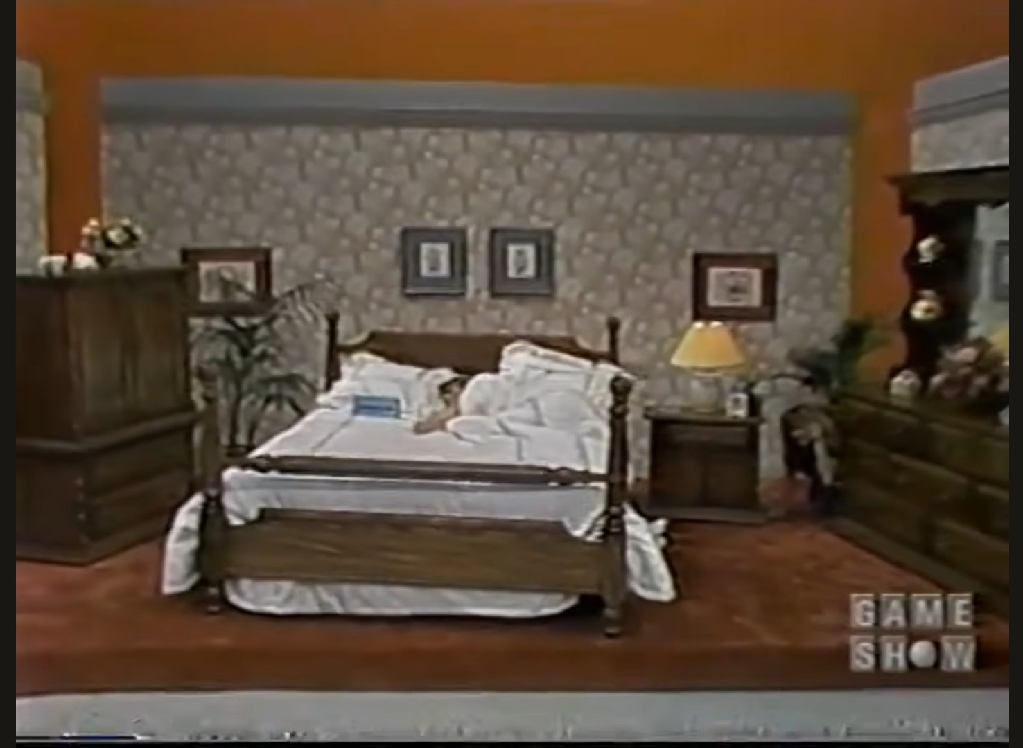 A bedroom set featuring a wooden bed with white bedding, nightstand with lamp, dresser, and decorative wall art.