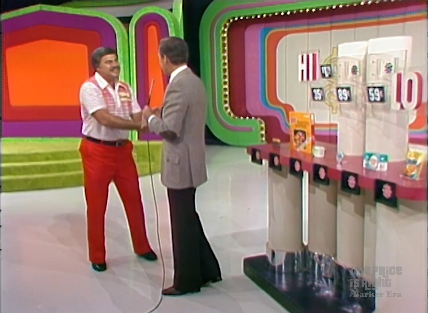 Contestant shakes hands with the host on the set of The Price is Right, ready to play the game Hi Lo, with grocery products displayed in the background.