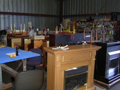 Interior view of a workshop with various furniture pieces, including a wooden fireplace, tables, and shelves filled with supplies.