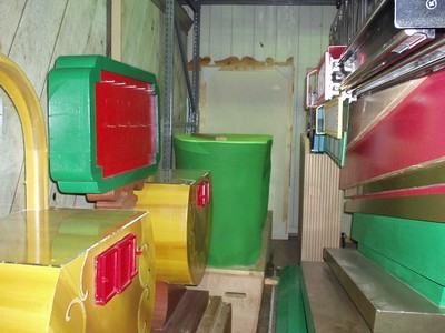 Storage area of colorful game props, including yellow boxes with red accents and a green container, against a backdrop of wooden walls and shelves.