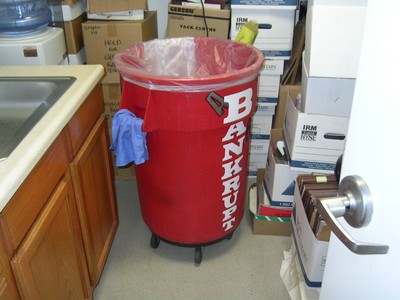 A large red trash can labeled 'BANKRUPT' from Wheel of Fortune located in a storage area filled with boxes backstage at The Price is Right.