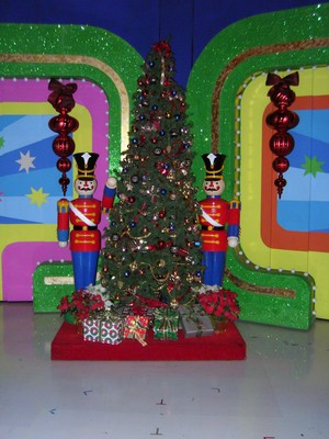 A festive Christmas tree adorned with ornaments and presents, flanked by two decorative nutcracker figures, set against a colorful backdrop.