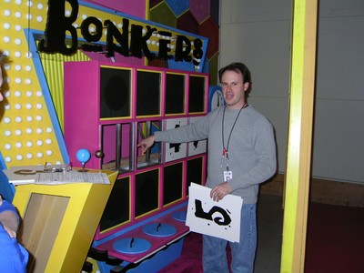 A man is interacting with the game "Bonkers" from a television game show, standing beside a colorful game board featuring multiple squares and a large title.