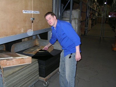 A person in a blue shirt is examining and organizing materials on a cart in a warehouse or studio environment.